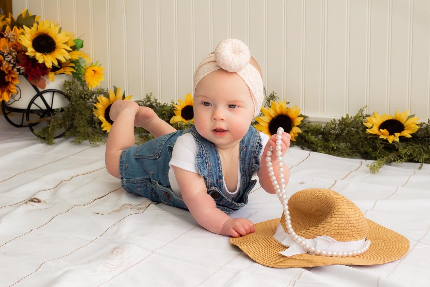 A baby laying on a blanket with a Lola, Blush - Bamboo Baby Knotted Headwrap from the Tiny Knot Co and sunflowers.