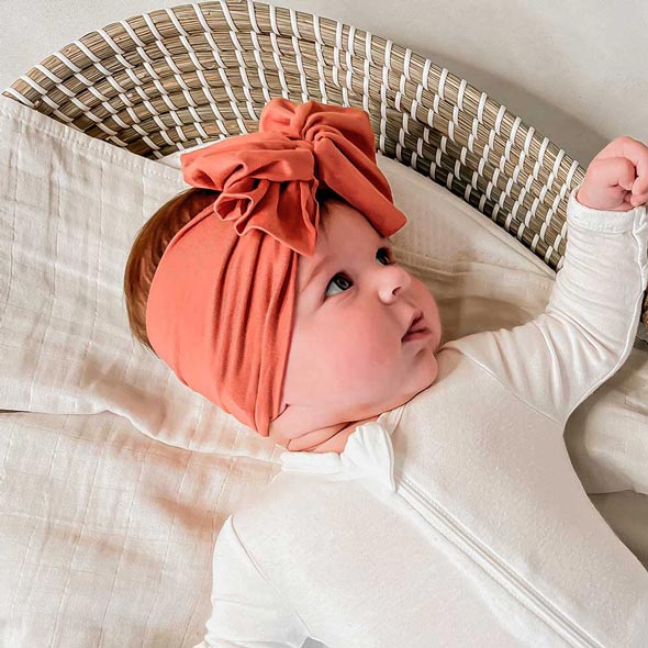 A baby is peacefully resting in a Tiny Knot Co wicker basket with a dainty headband.