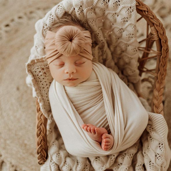 A newborn sleeping in a wicker basket with a Tiny Knot Co headband.