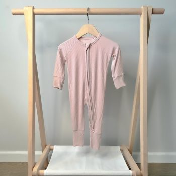 A Tiny Knot Co pink sleepsuit hanging on a wooden rack.