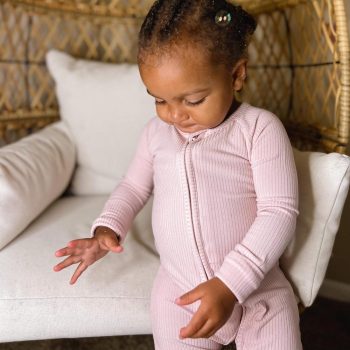 A tiny baby girl in a pink pajama sitting on a chair, featuring Tiny Knot Co.