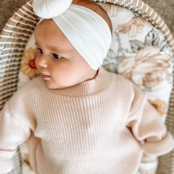 A baby in a wicker basket wearing the Snow - Bamboo Baby Knotted Headwrap from Tiny Knot Co.