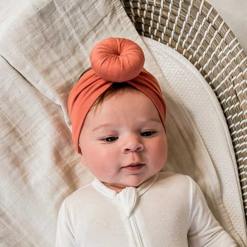 A Tiny Knot Co newborn wearing an Ember - Bamboo Baby Knotted Headwrap in a wicker basket.