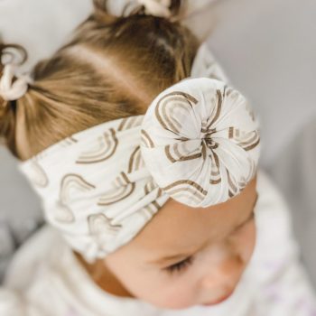 A little girl wearing the Tiny Knot Co - Ellie Bamboo Baby Knotted Headwrap with a flower on it.