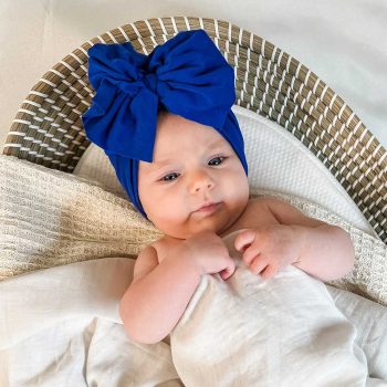 A Tiny Knot Co baby wearing a blue bow hat nestled in a basket.