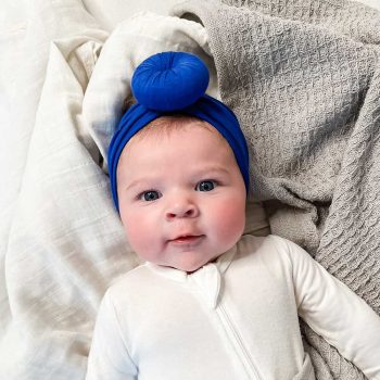 A Tiny Knot Co baby wearing a blue turban is peacefully laying on a blanket.